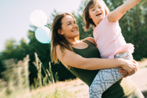 A mother holding their disabled child on a sunny day in a field while they both laugh and play